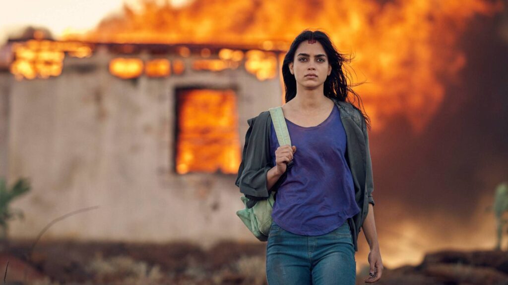 Melissa Barrera walking in front a backdrop of flames
