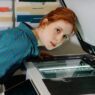 A red headed women with her face hovering above a photocopy machine.