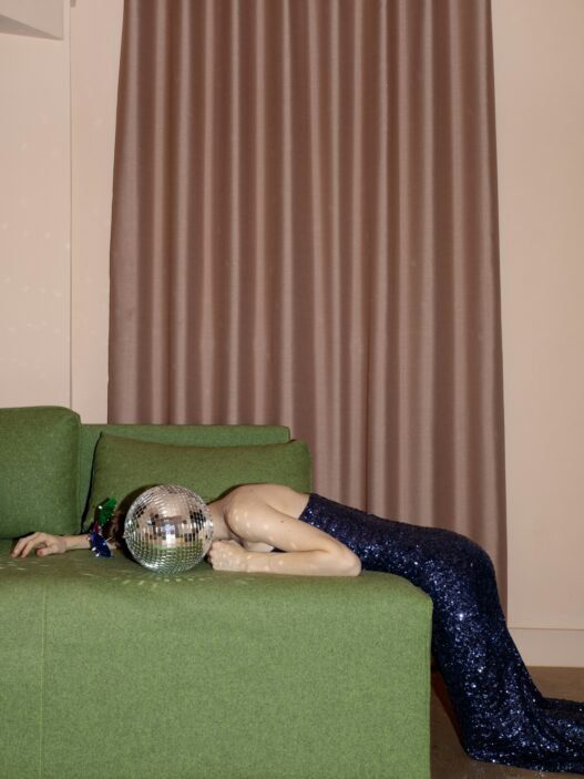 A person in a squint dress laying on a green couch with a disco covering her face.